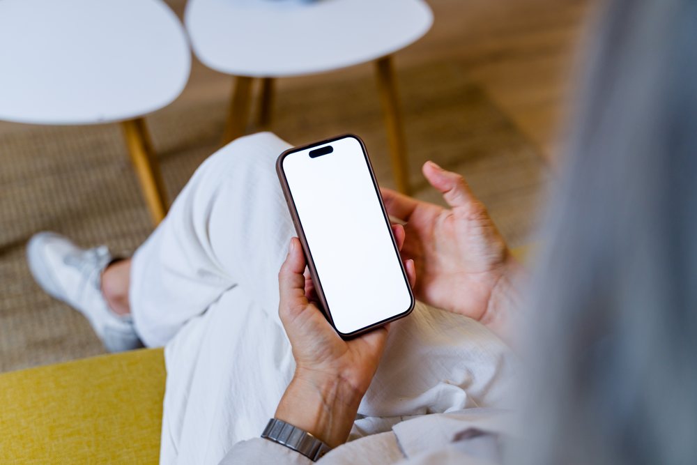 Person seated indoors holding a smartphone with a blank white screen near white round tables, Spain.