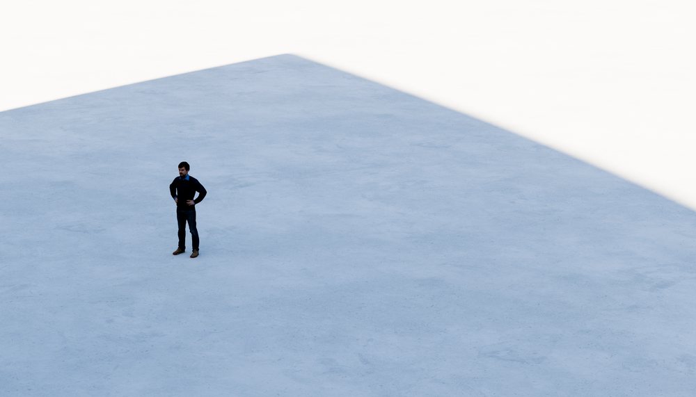 A man standing alone on a large concrete floor with shadow