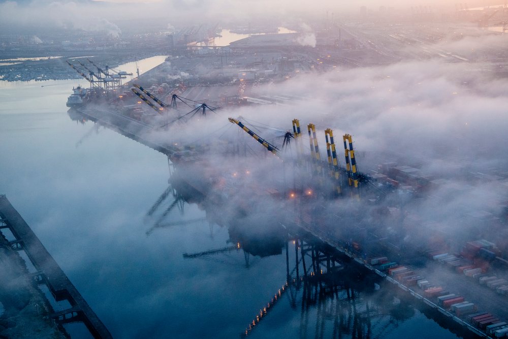 Cargo cranes and container ships partially obscured by fog at a major port in lifornia, Port of Long Beach, CA, USA.