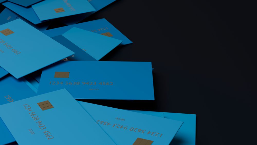 Stacked blue credit cards with chip and visible numbers on a dark surface.