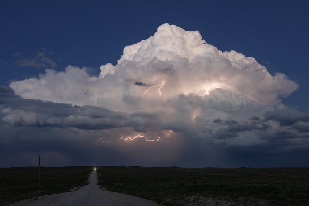 Lightning flashes illuminate a dense Supercell thunderstorm over a rural road at night, Storm Chasing, Nara Visa, New Mexico, USA.