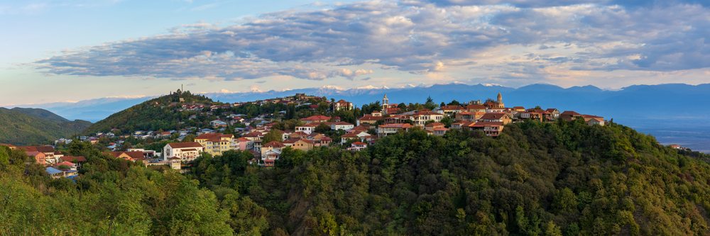 Sighnaghi town nestled on a hillside with orange rooftops and green forests, backed by the Caucasus Mountains at Sunrise, Georgia.