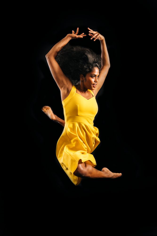 Woman jumping mid-air in a yellow dress against a dark background, showing dynamic movement and energy.