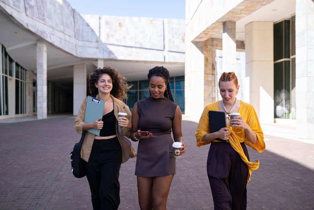 Group of women walking outdoors in an urban setting, holding disposable coffee cups and a mobile phone, Spain.