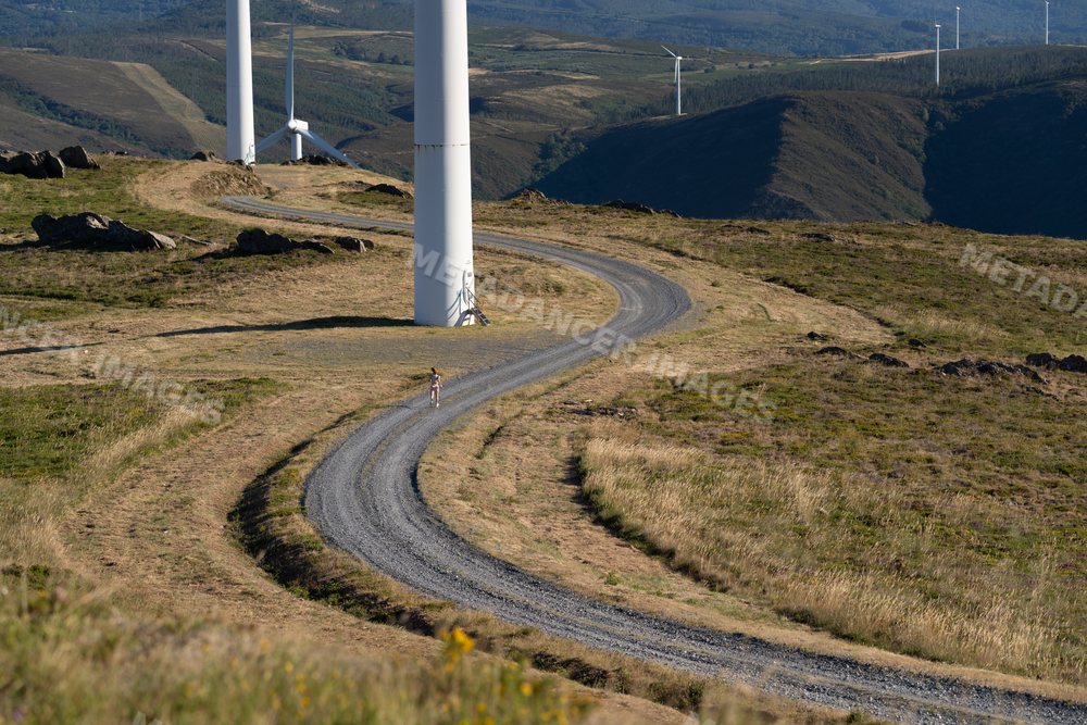 A white woman running on a trail by wind turbines in Galicia, Spain