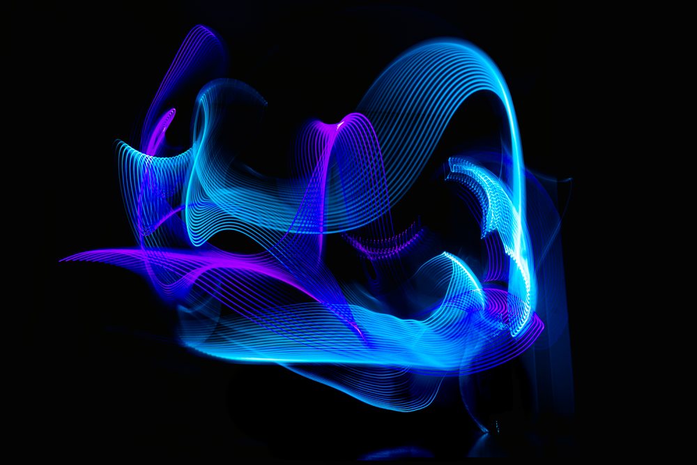 Light painting creates abstract curved blue and purple LED ribbons on a dark background using long exposure.