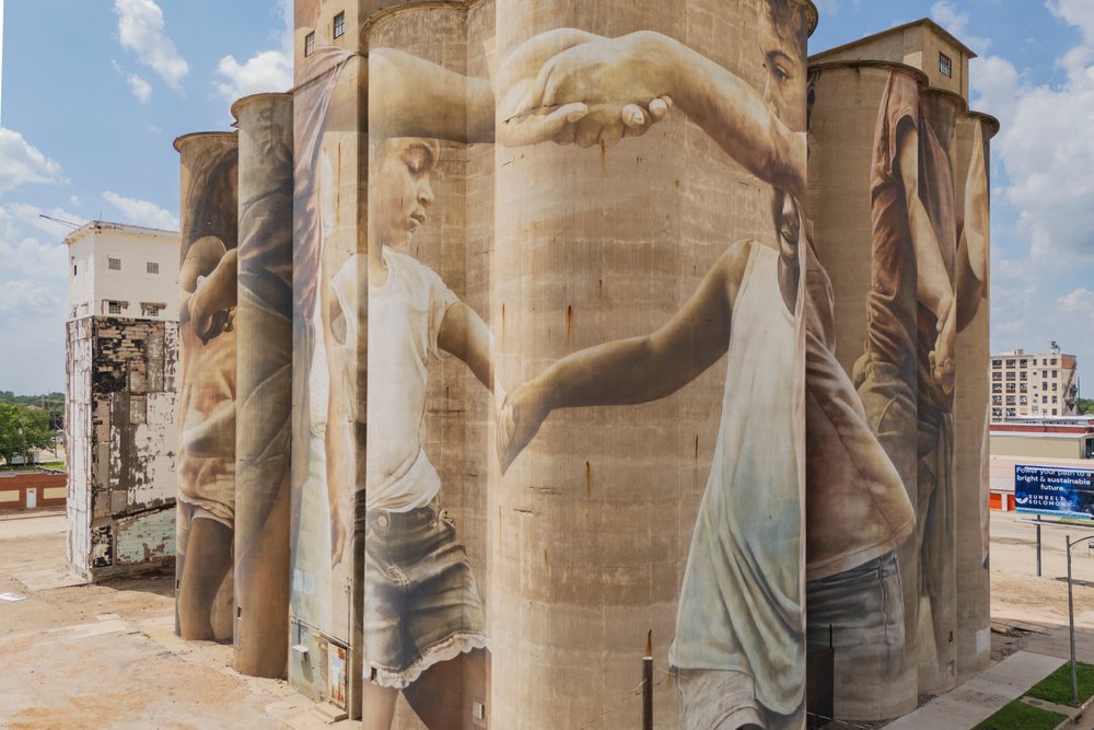 Grain Silo, features a large mural of children holding hands on its concrete facade under a partly cloudy sky, Storm Chasing, Weather, Environmental Issues, Salina, Kansas, USA.