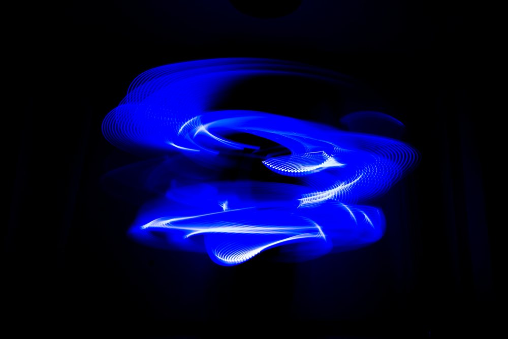 Blue light painting showing swirling LED light patterns captured in long exposure photography against a dark background.