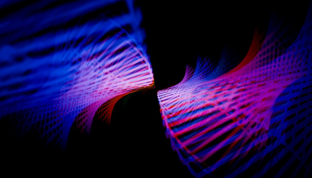 Abstract colorful light trails in blue and pink create dynamic wave shapes on a black background.