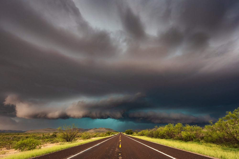 Dark storm cloud forms over a straight paved road with dense shrubs near Sanderson in the Texas Great Plains, USA.