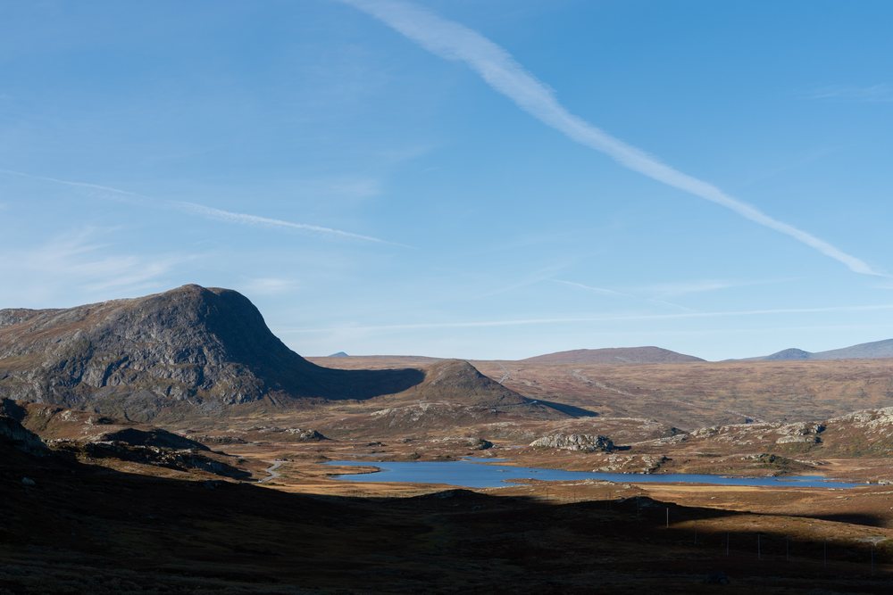 Serene mountain landscape with a rocky terrain and a lake under a clear blue sky, Norway.