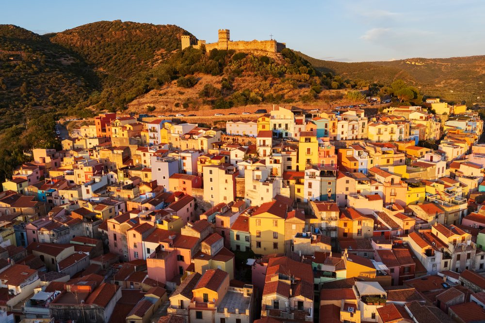 Colorful houses cluster beneath a hilltop castle at Sunset in Bosa's Old Town, Travel Images, Sardinia, Italy.
