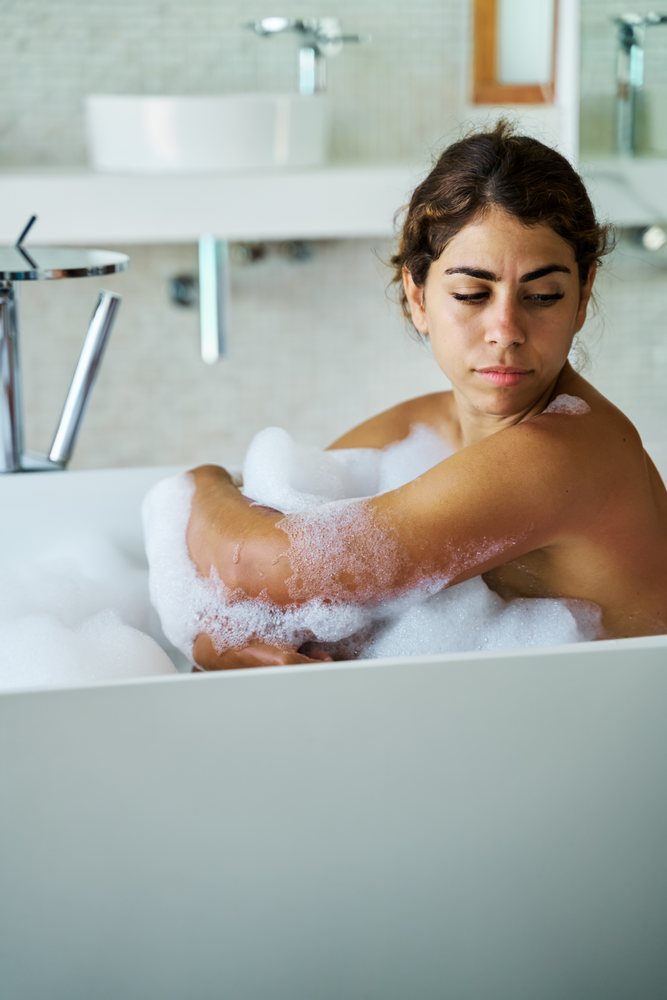 A woman is relaxing in a bathtub filled with bubbles inside a modern bathroom in the, Maldives.