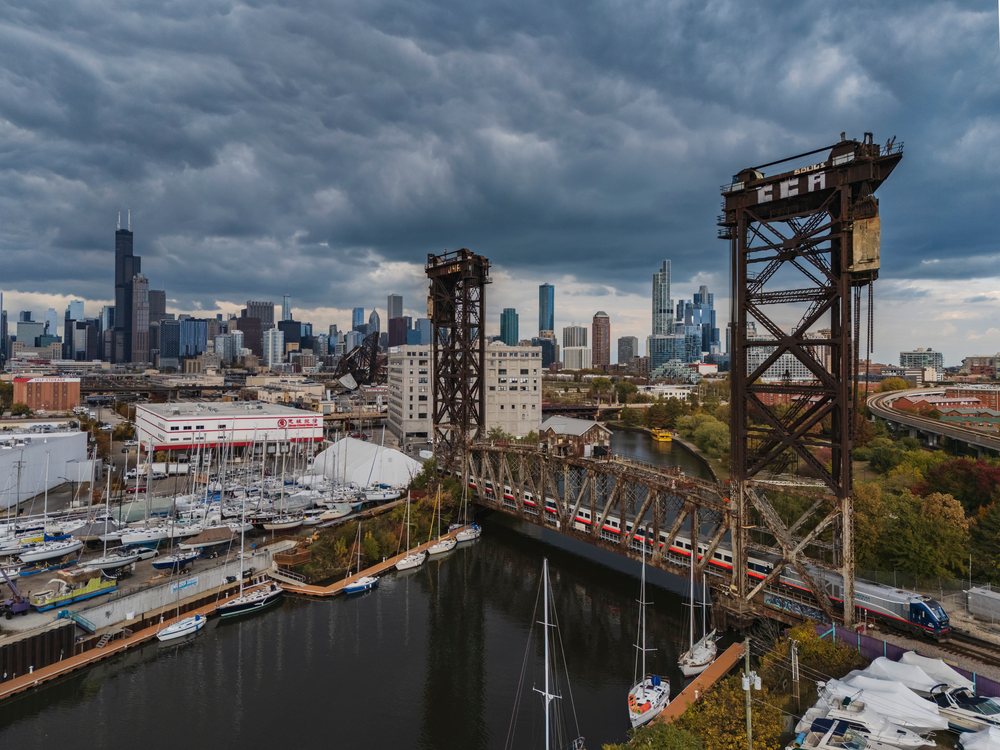 Canal Street railway lift bridge spans a waterway with a train crossing and Chicago skyline under cloudy skies, Americana, Historic, Illinois, USA.