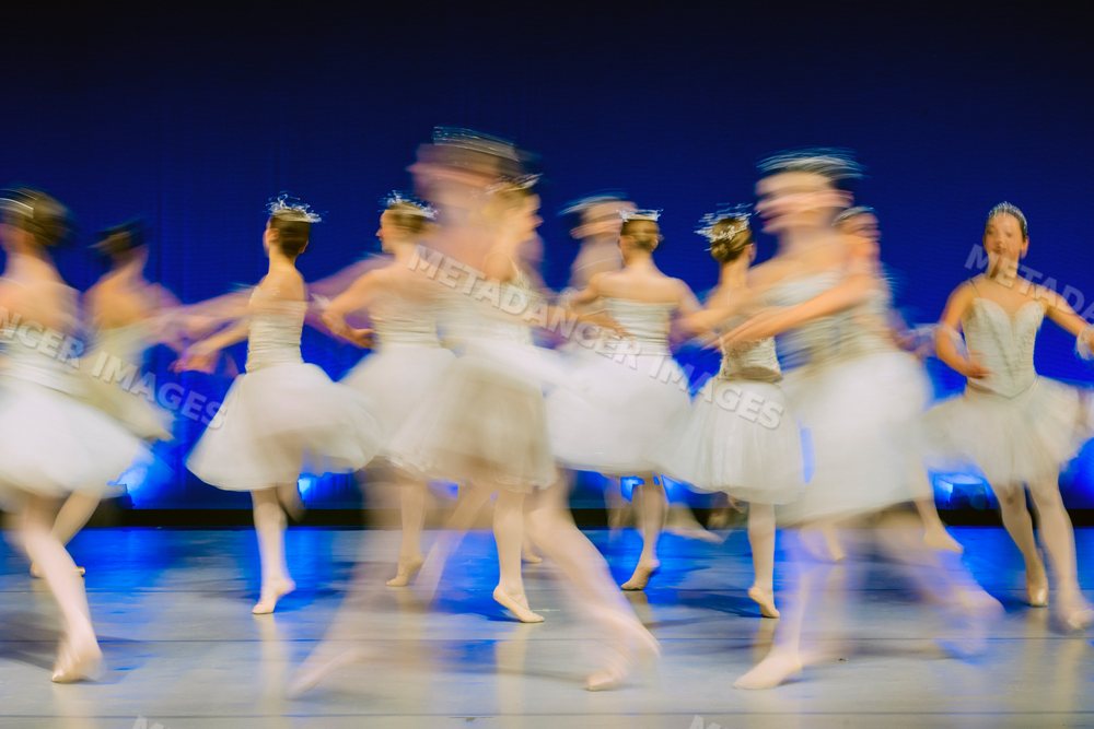 Female ballet dancers perform a group dance on stage in white tutus