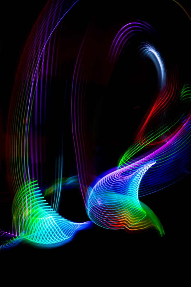 Swirling and streaking colorful LED light patterns form an abstract painting against a dark background.