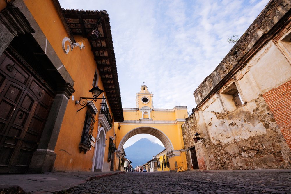 Volcan de Agua volcano seen through a historic yellow archway in Antigua, Guatemala under a cloudy sky, Sacatepequez Department.