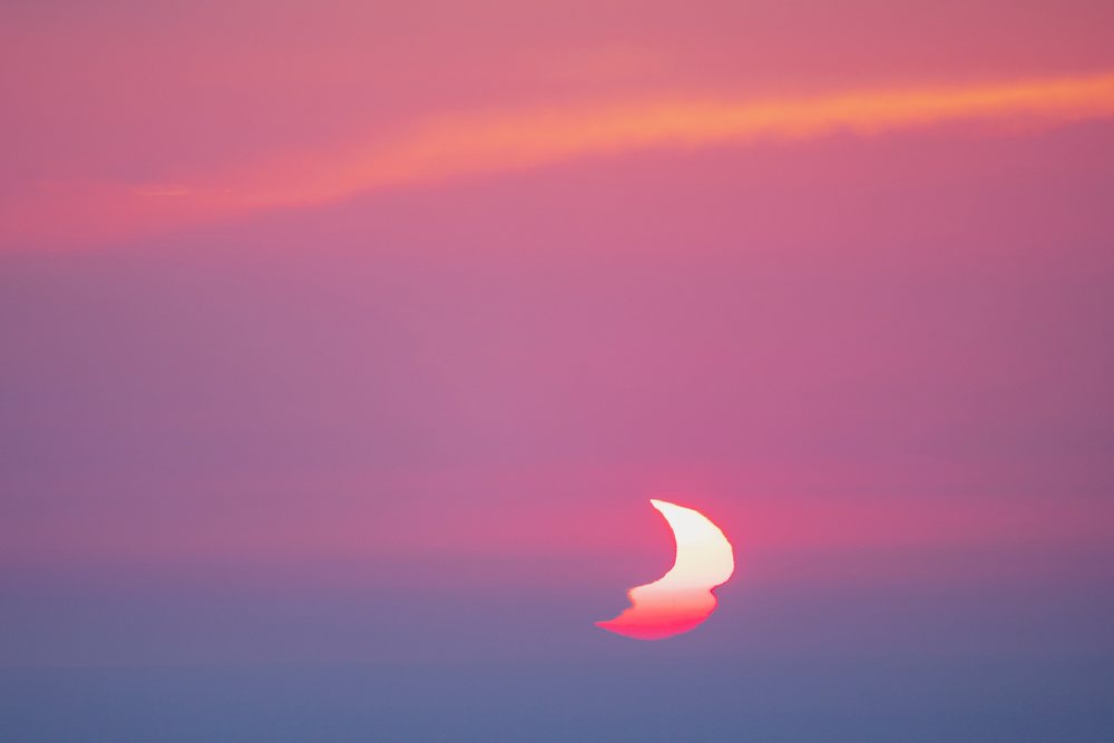 Sunset with a partially eclipsed Sun and pink and purple clouds over Valldemossa, in a serene natural landscape, Mallorca, Spain.