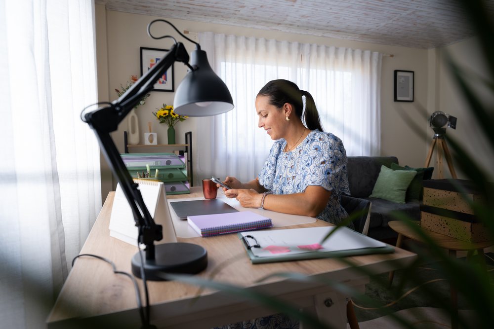 Woman telecommuting at her home office desk using a smartphone, Spain.