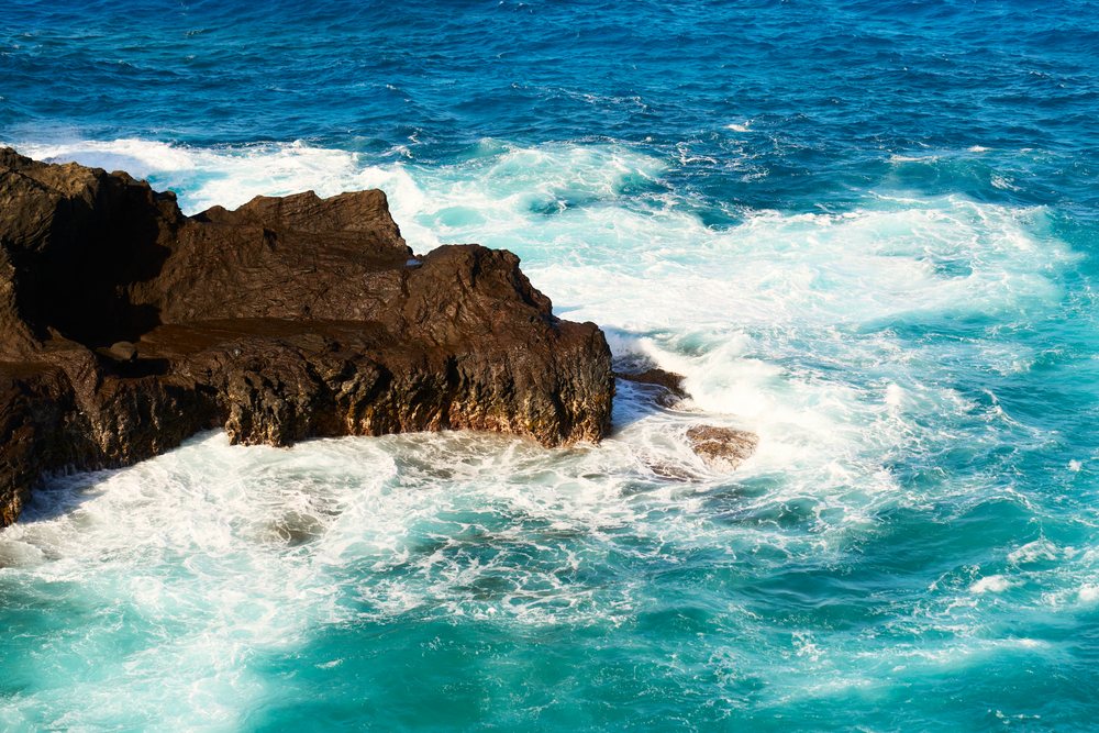 Ocean waves crashing against the rocky coastline with foamy surf and vibrant blue water, Oahu, Hawaii, USA.