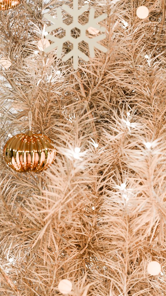Christmas tree decorated with gold ornament ball, white lights, and snowflake decoration for winter holiday celebration.
