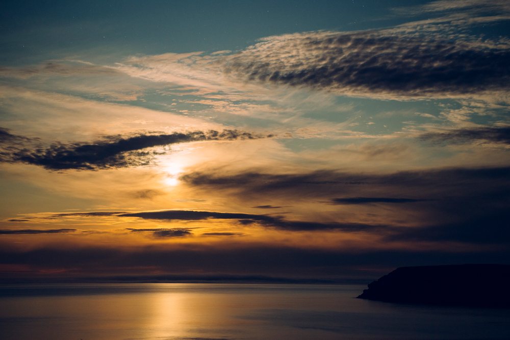 Sunset over ocean with reflections and dramatic clouds near a coastal cliff, Meyers Creek, Oregon, USA.