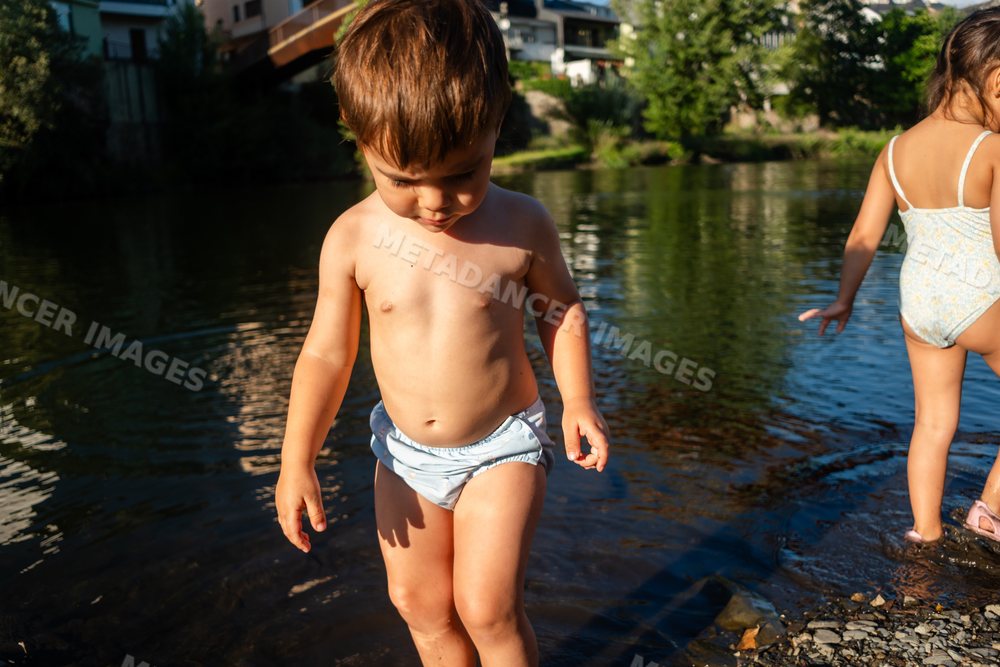 A toddler white boy wading in a shallow river on a sunny summer day