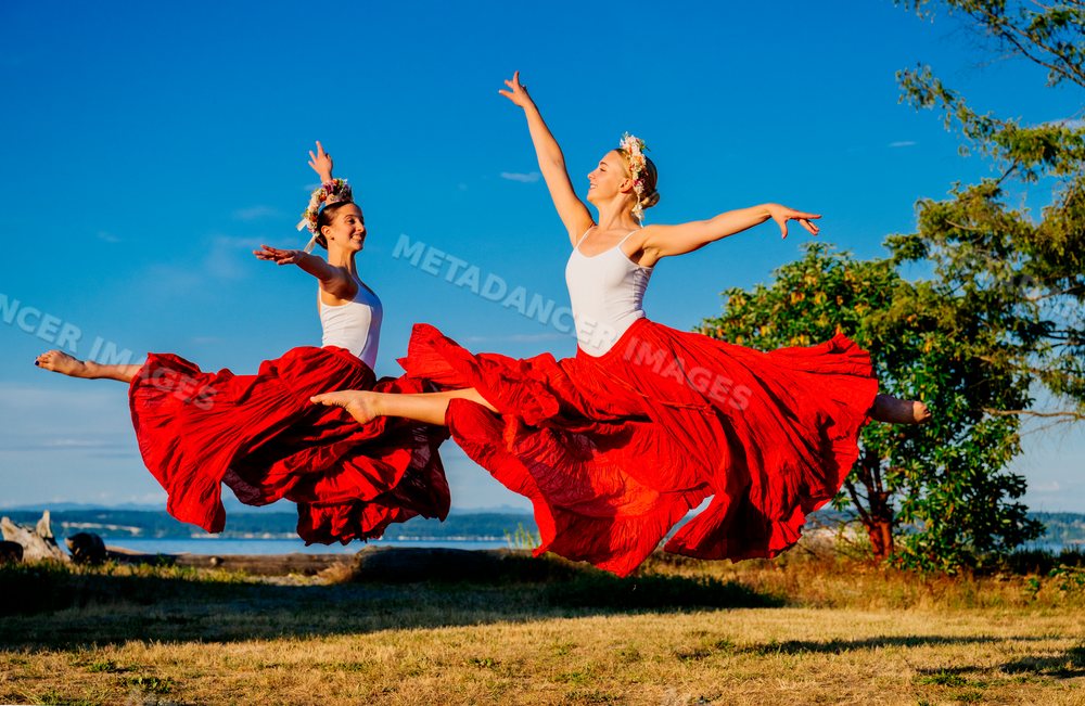 Two white women jump gracefully outdoors wearing red skirts and flower