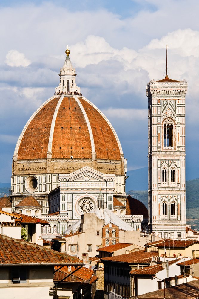 Santa Maria del Fiore cathedral dome and bell tower rise above Florence rooftops under a partly cloudy sky, Italy.