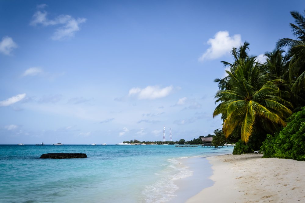 Tropical beach scene with turquoise ocean water, white sand, palm trees, boats on the water, and a pier under a blue sky, summer, Holliday, travel, landscape, Maldives.