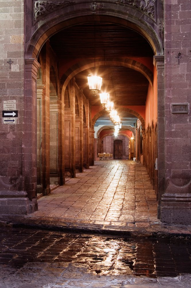 Stone floor walkway with lantern lighting under arches and pillars, San Miguel de Allende, Mexico.