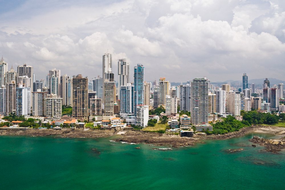 Panorama showing Panama city skyline with high-rise buildings along a bay under a cloudy sky.