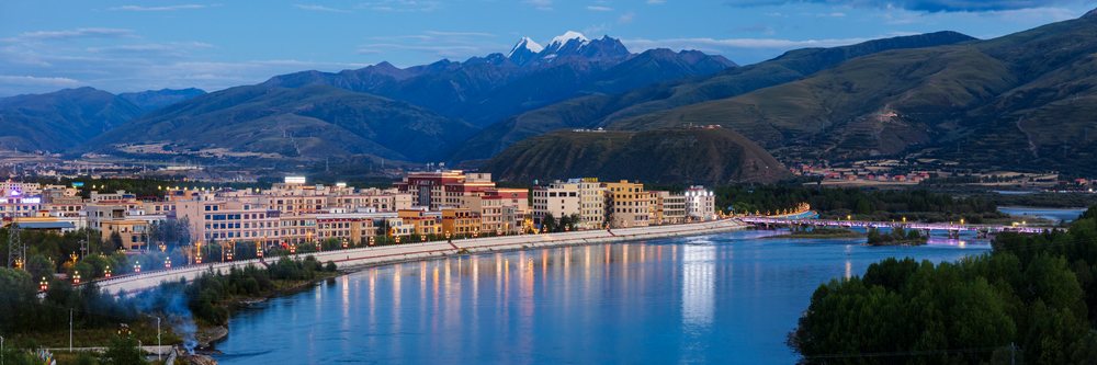 View of Garze city along the River with Kawaluori Mountain and snow-capped peaks in the background at Dusk, China, Sichuan Province, People's Republic of China.