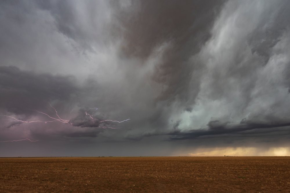 Lightning bolts strike beneath dark storm clouds over a flat open field, Storm Chasing, Weather, Environment, Floydada, Texas, USA.