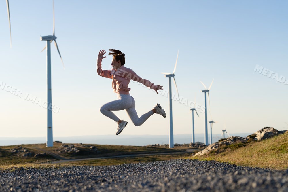 A white woman jumps actively near wind turbines in Galicia Spain