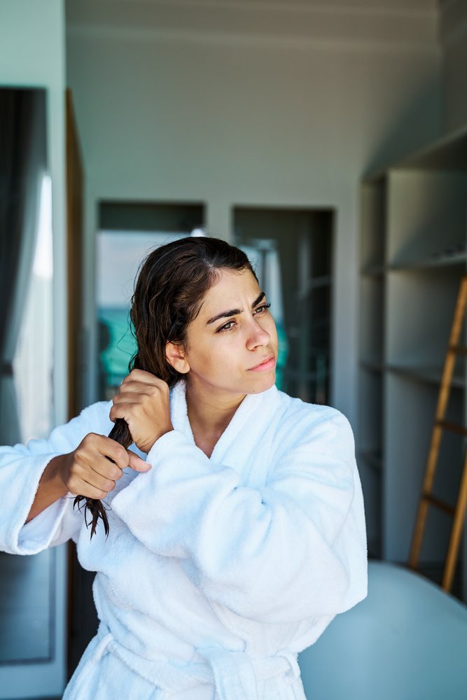 A woman wearing a white bathrobe combs her wet hair indoors in a home bathroom setting in the, Maldives.