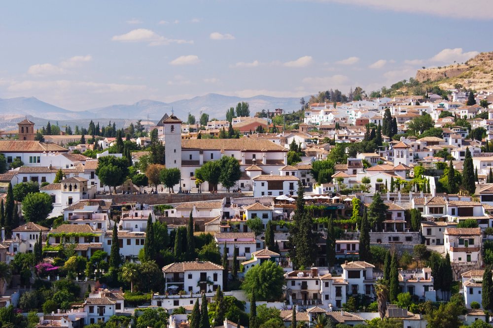 Mediterranean town with white houses and red tiled roofs set against mountains on a sunny day, Andalucia, Spain.