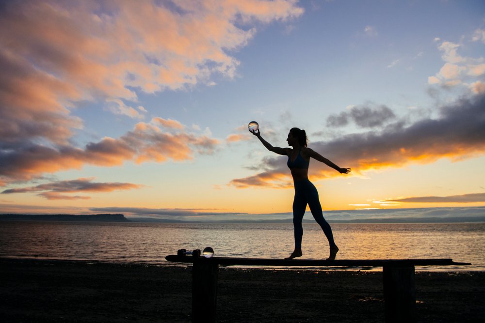 Silhouette of a woman balancing on a board holding a crystal ball at sunset on a beach, WA, USA.