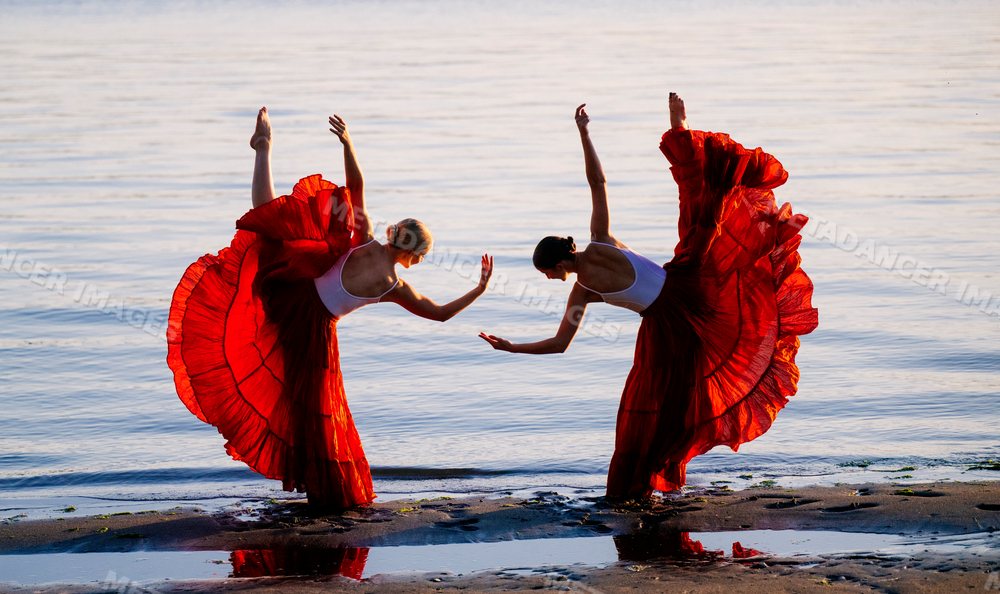 Two white women performing partner acrobatics yoga on a beach