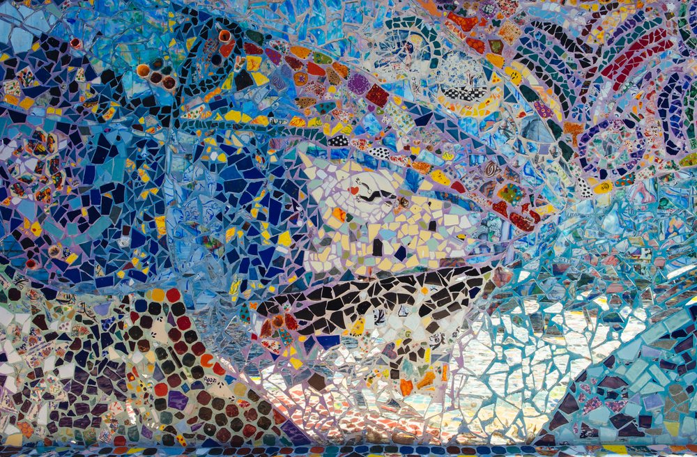 Colorful mosaic artwork composed of broken tile pieces and glass forming an abstract pattern with dominant blue, purple, and orange hues, CA, USA.