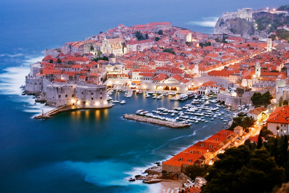 Historic old city of Dubrovnik showing medieval stone walls, harbor boats, and red tile roofs by the sea, Dusk, Croatia.