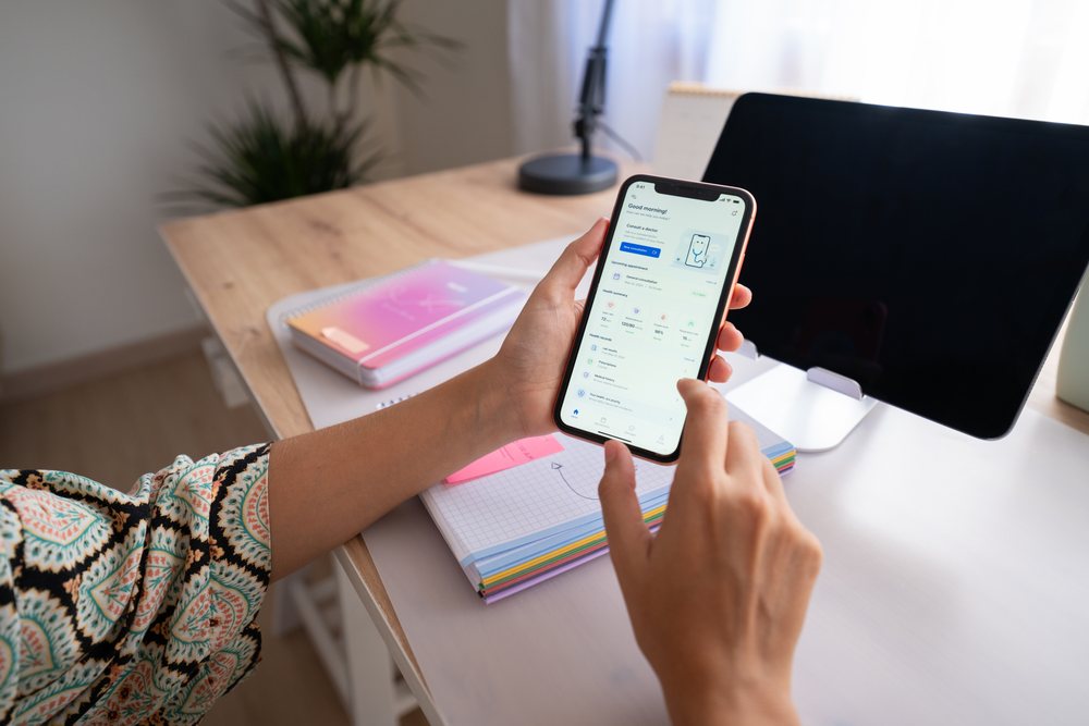 Woman holding smartphone showing a digital health app in a modern home office workspace, Spain.