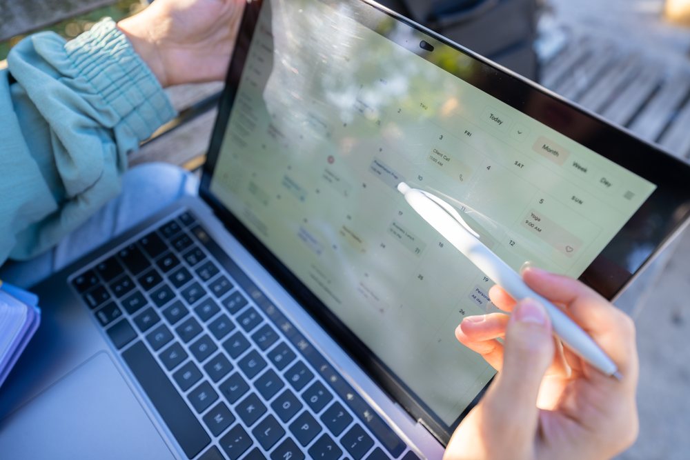 Person outdoors holding a stylus and using a digital calendar interface on a tablet laptop for schedule planning, Spain.