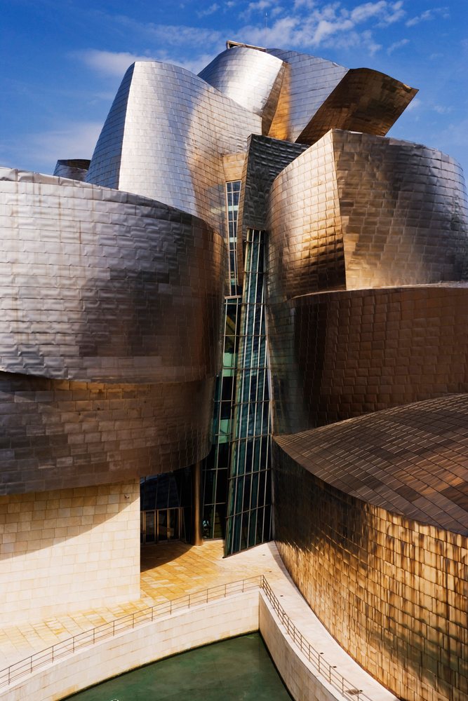 Guggenheim Museum, Spain features a curved metal exterior and glass entrance under a clear blue sky, Bilbao.