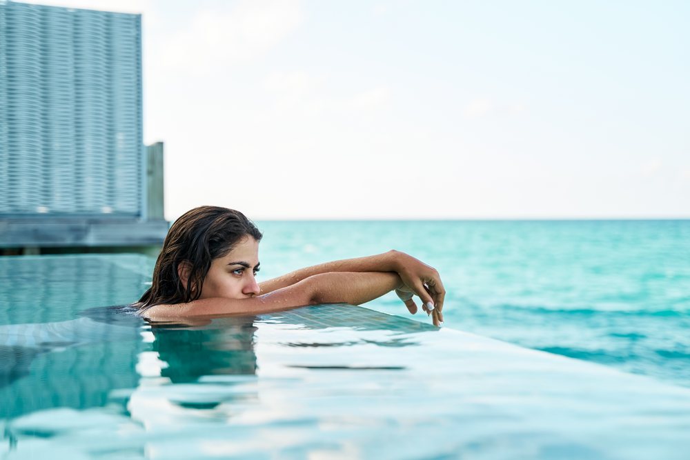 A white woman relaxes in an infinity pool overlooking the sea