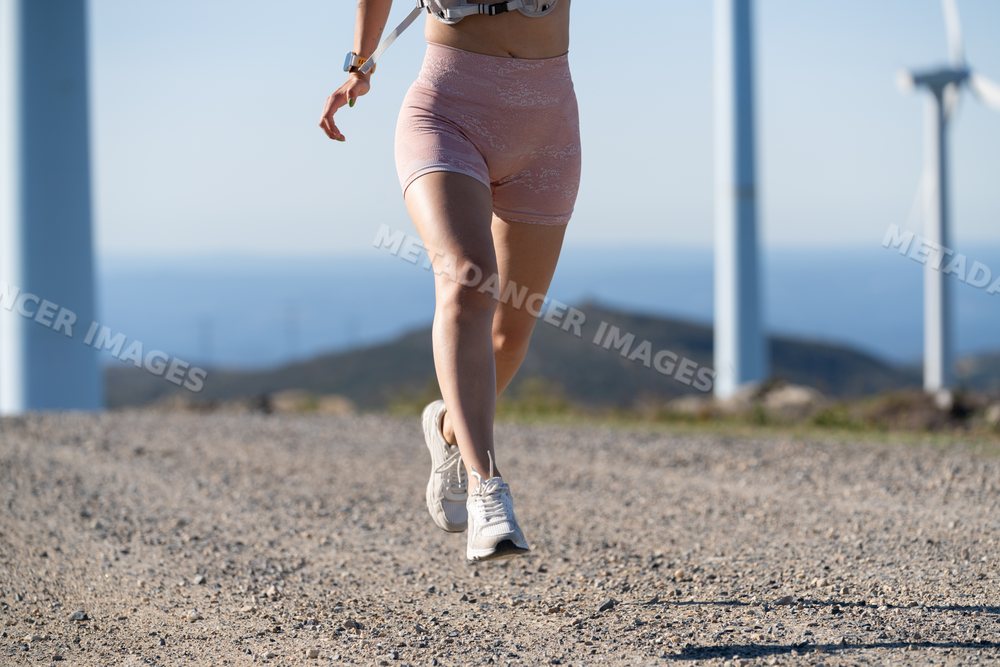 White Woman running on a gravel trail near wind turbines in Galicia