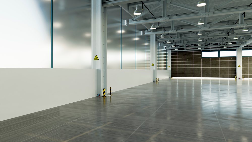 Large empty industrial warehouse interior with polished concrete floor, multiple steel columns, overhead lighting, and a closed loading bay door, car, manufacturing, industry.