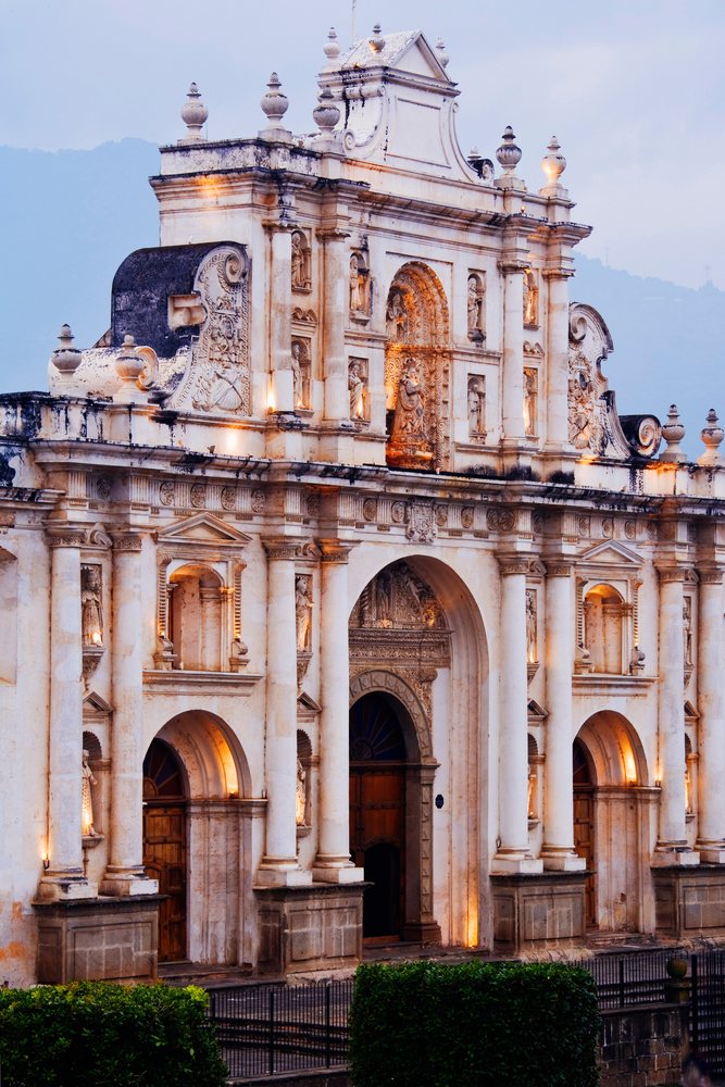 The stone facade of Catedral de San Jose, showcases detailed sculptures and columns illuminated, Dusk, Antigua, Guatemala.