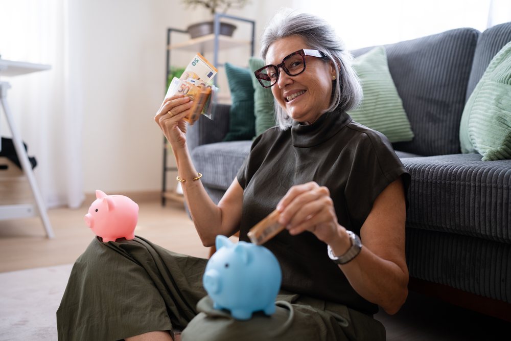 Woman saving euro banknotes in piggy banks in living room, Spain.