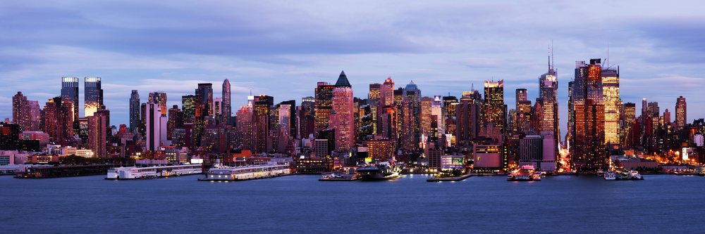 Manhattan skyline and waterfront at dusk with high-rise buildings and lights reflected on the river surface, New York, USA.
